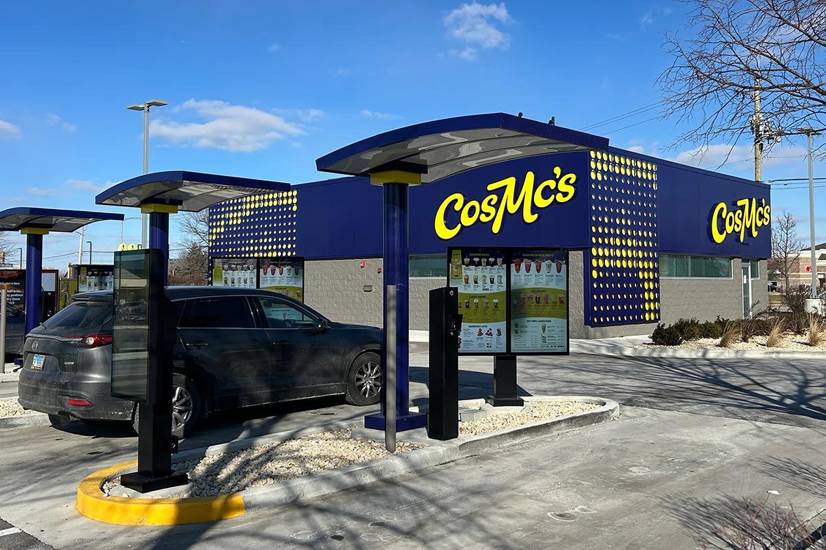 Exterior of a blue CosMc's restaurant with a drive through and order menu in the foreground