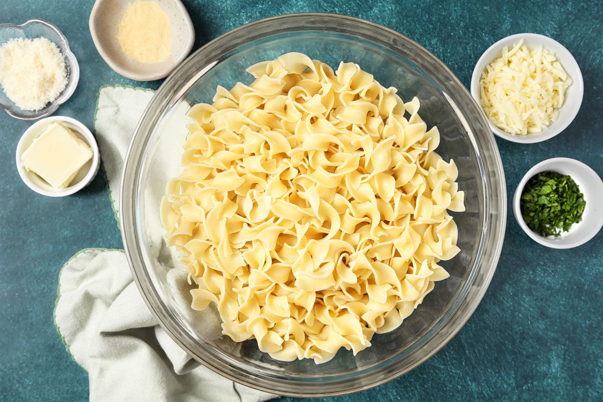 Overhead shot; Cook noodles according to package directions; drain; Transfer cooked noodles in a large glass bowl; napkin; teal green surface;