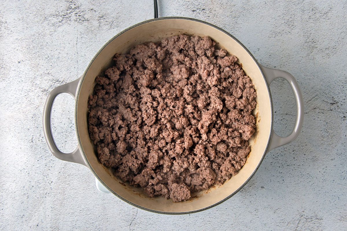 overhead shot of a large, round pot with two handles, filled with ground beef that has been cooked; the pot is sitting on a light gray countertop;