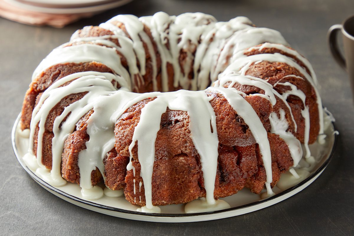 closeup shot of monkey bread on a white plate; a creamy white icing is drizzled over the top, the plate sits on a dark colored countertop with a subtle marble pattern