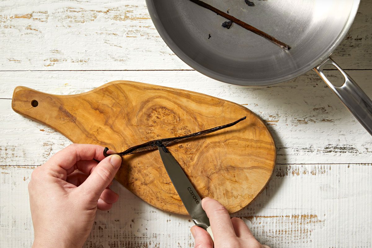Overhead shot of split vanilla bean lengthwise; Using the tip of a sharp knife; scrape seeds from the center into a small saucepan; add bean; wooden surface;