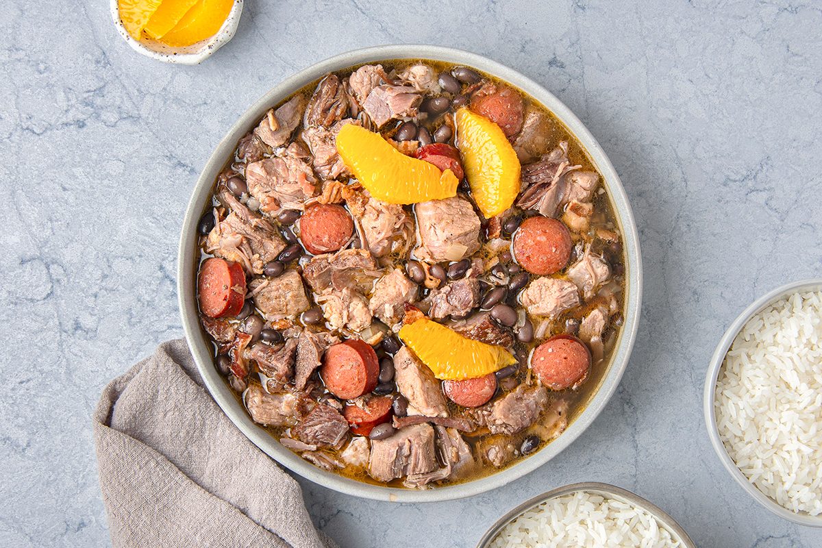 A bowl of feijoada, a Brazilian stew containing black beans, pork, and sausage, garnished with orange slices. 