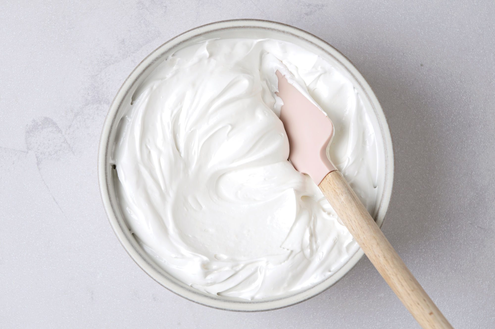 Overhead shot of Fluffy White Frosting; in a large bowl; spatula; marble surface;