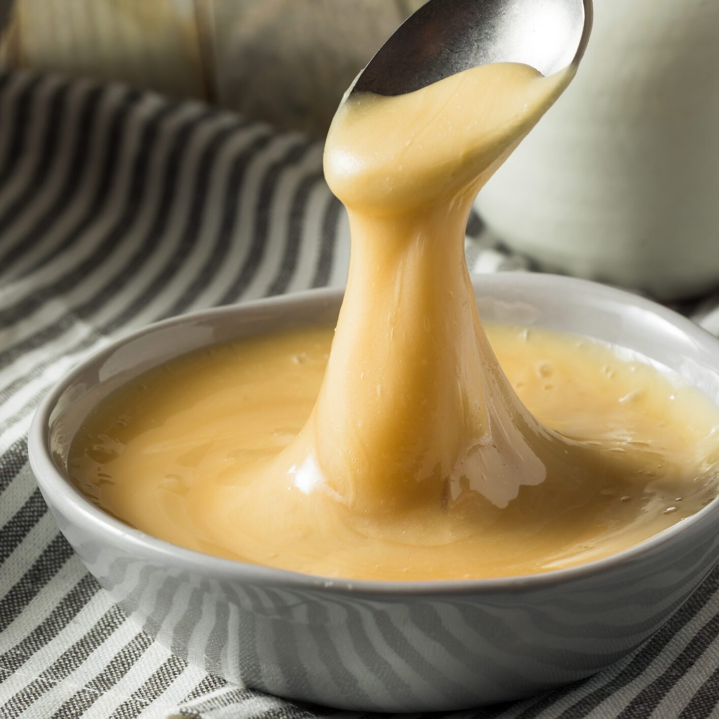 Spoon drizzles whipped honey into a white bowl on a striped kitchen towel