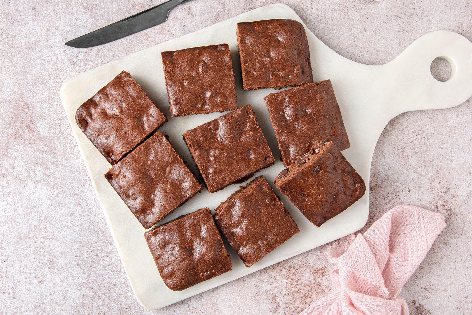 Overhead shot of Easy Gluten Free Brownies; place on white tray; knife; napkin; light brown marble surface