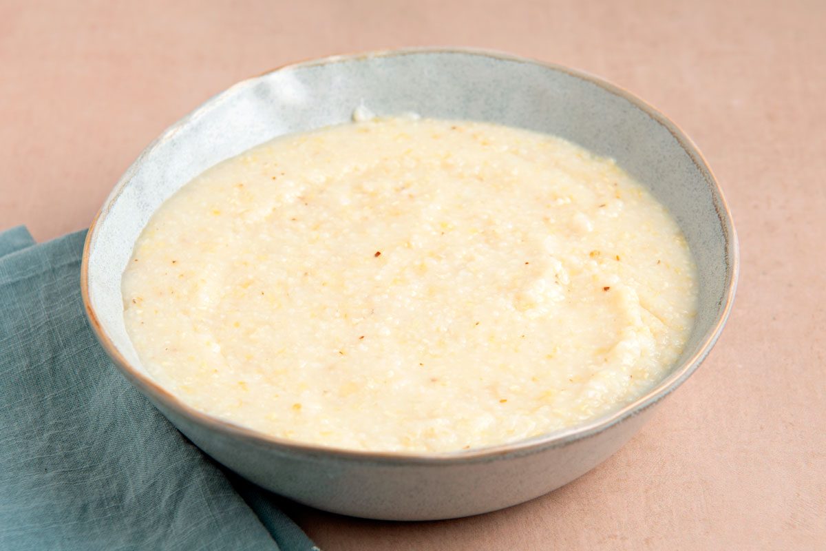 a close-up of a bowl of creamy white porridge, likely grits or polenta, sitting on a light brown surface with a light blue napkin