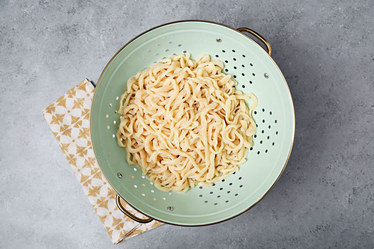 Cooked noodles draining in a strainer.