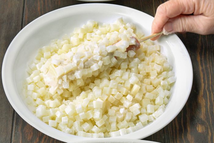 Rolling the hot dog and cheese skewer into cubed potatoes