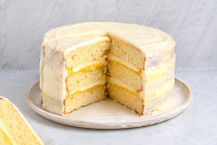 Wide shot of Lemon Curd cake with a slice taken out kept on top of a grey marbletop.