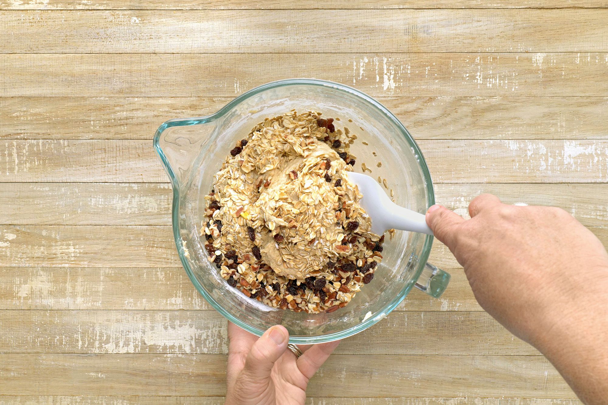Overhead shot of stir in the oats; raisins and pecans; wooden surface;