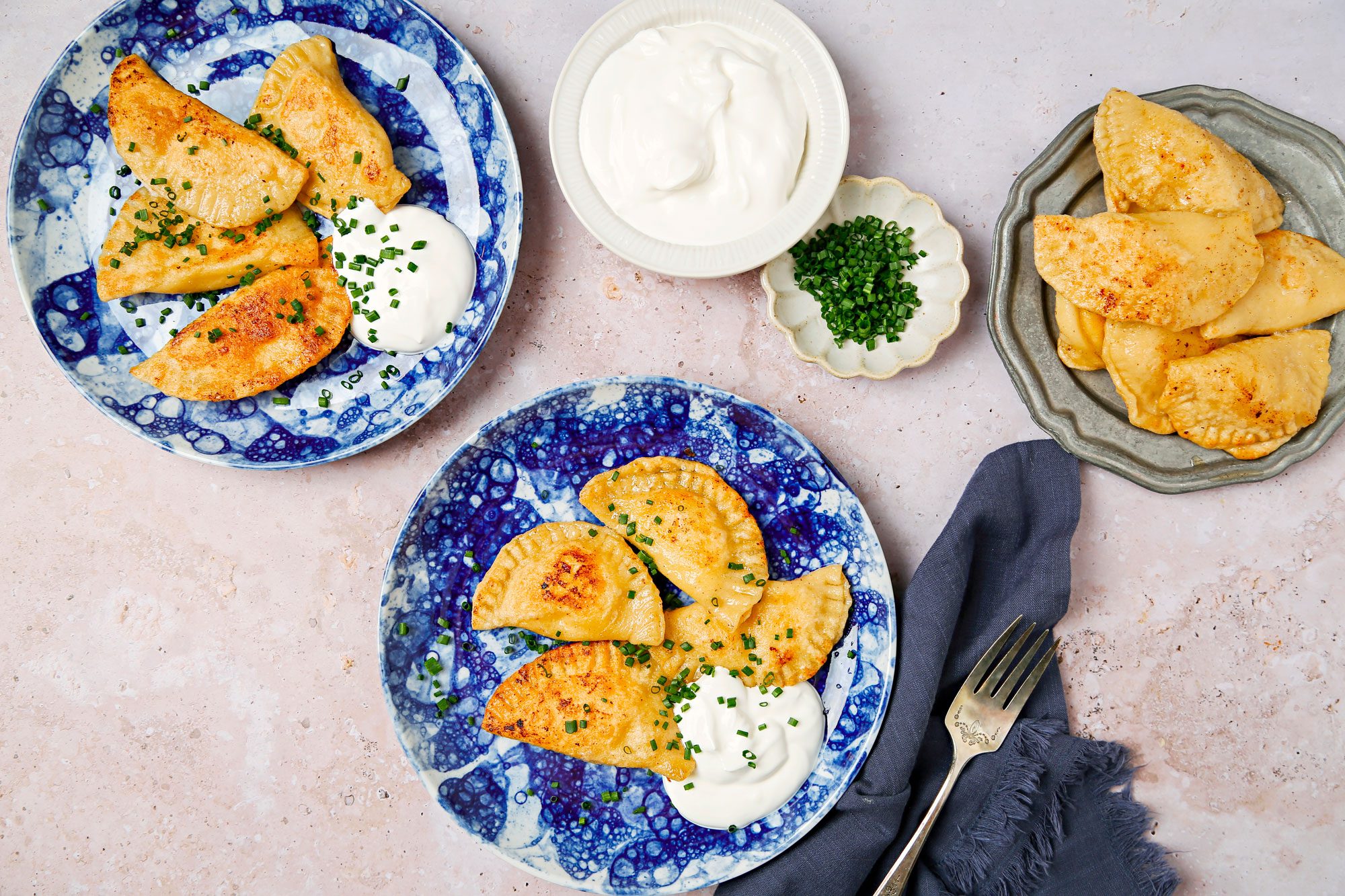 Sauteed pierogi served on blue and white plates with sour cream and chives