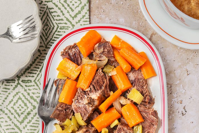 Sauerbraten sliced and served on a platter with vegetables and sauce on the side