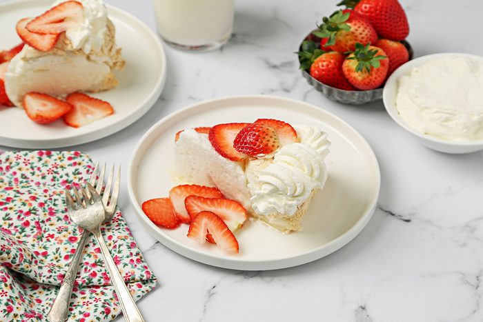 Schaum Torte with dollops of whipped cream and freshly chopped strawberries