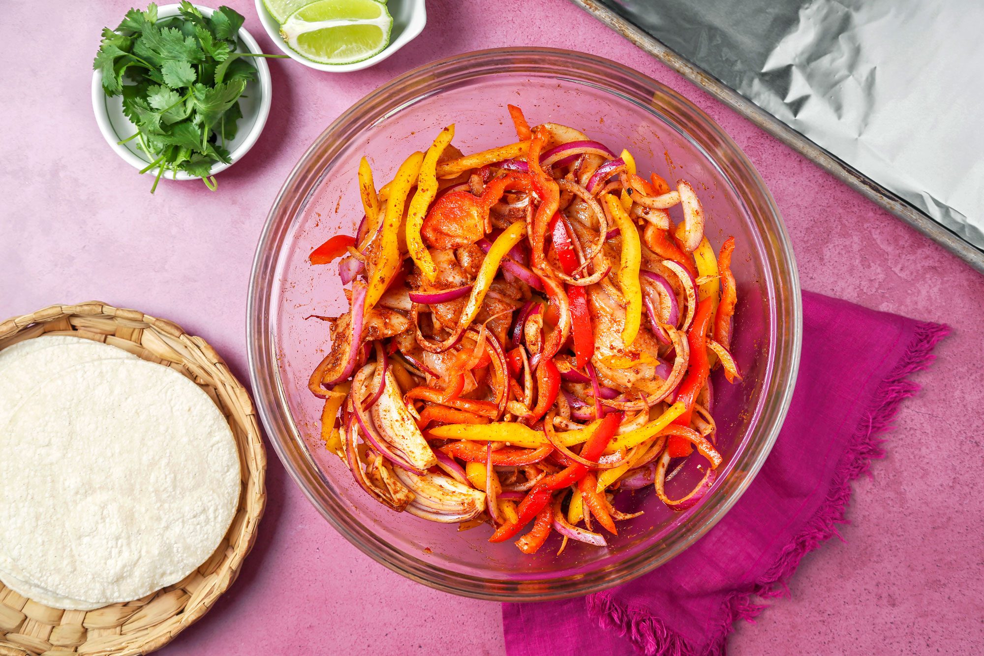 Chicken and peppers in a large bowl tossed with oil and seasonings