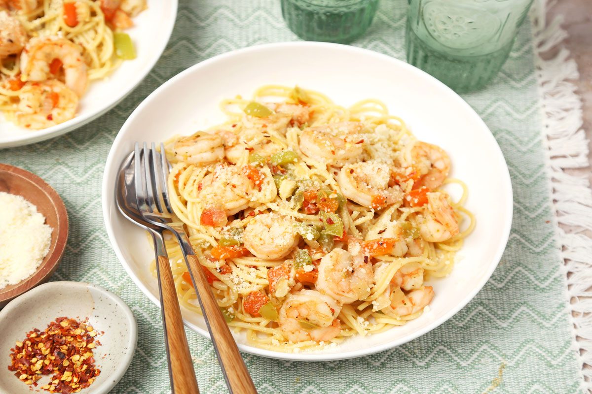 Shrimp Spaghetti shot on a beige marble surface. Pasta served in white bowls with parmesan and crushed red pepper flakes; 3/4th