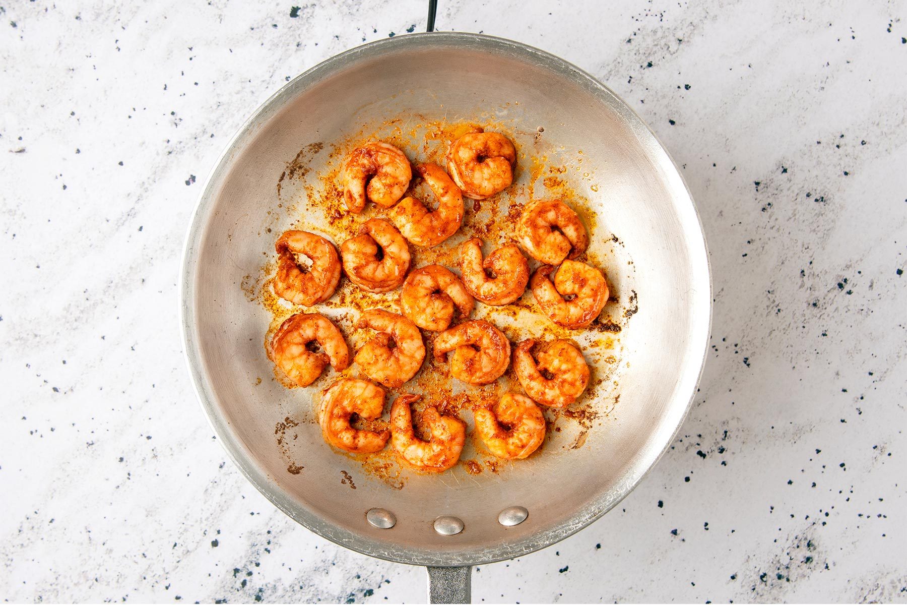 overhead shot of of a silver frying pan filled with cooked shrimp