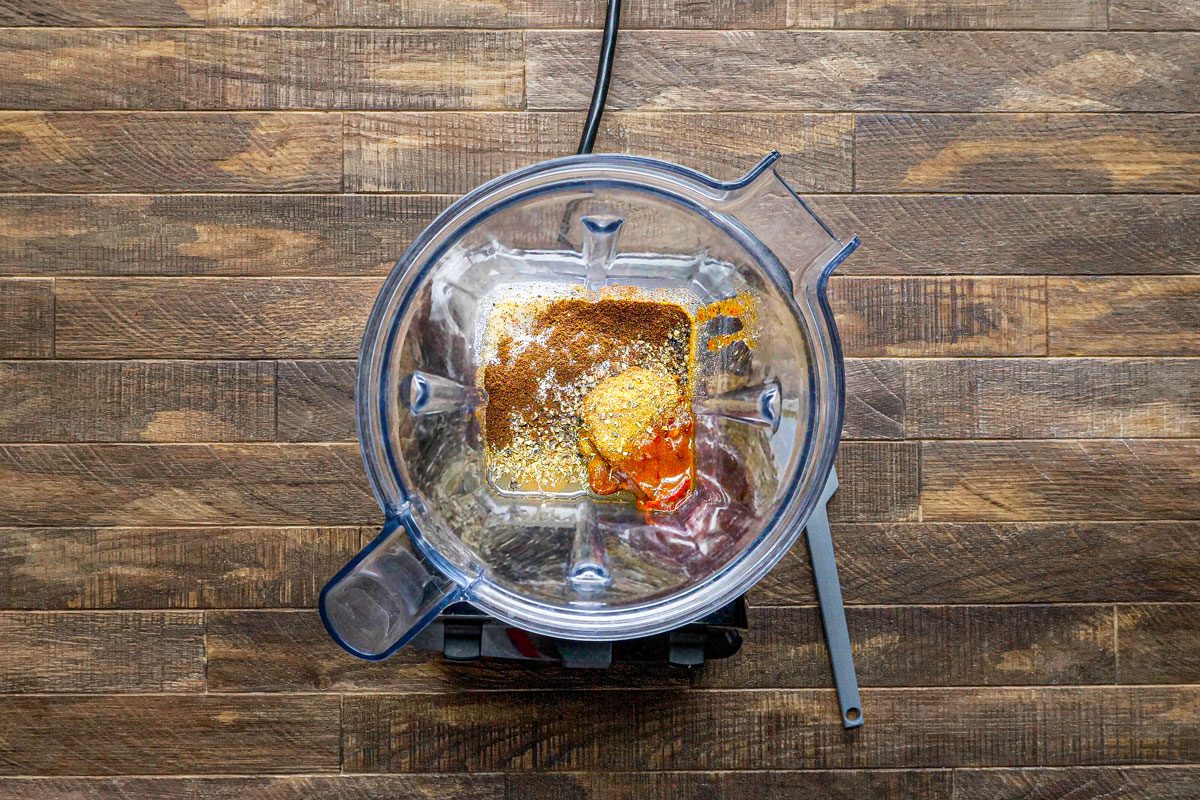overhead shot of a blender on a wooden countertop; inside the blender is a mixture of spices