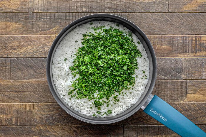 overhead shot of a black, oval-shaped frying pan on a wooden surface, filled with white rice and chopped parsley; the rice is covered in a generous amount of chopped parsley
