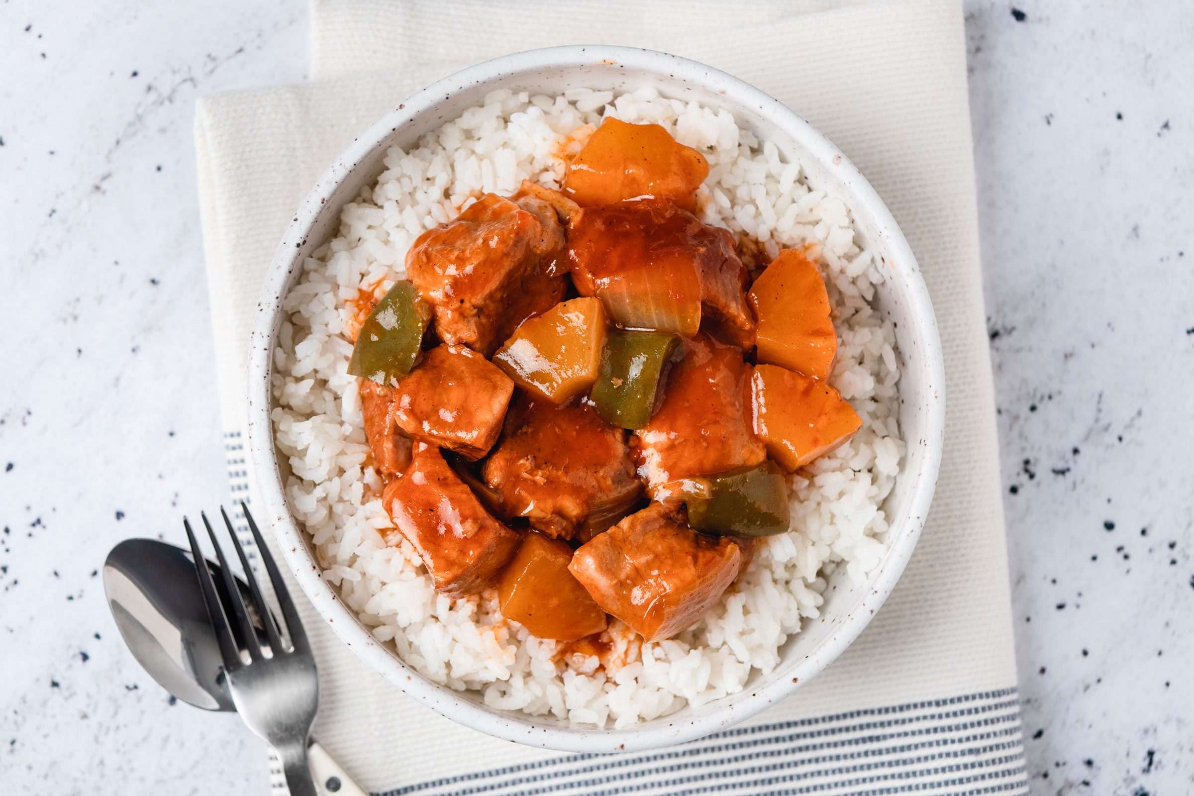Slow Cooker Sweet And Sour Pork poured over rice in a bowl