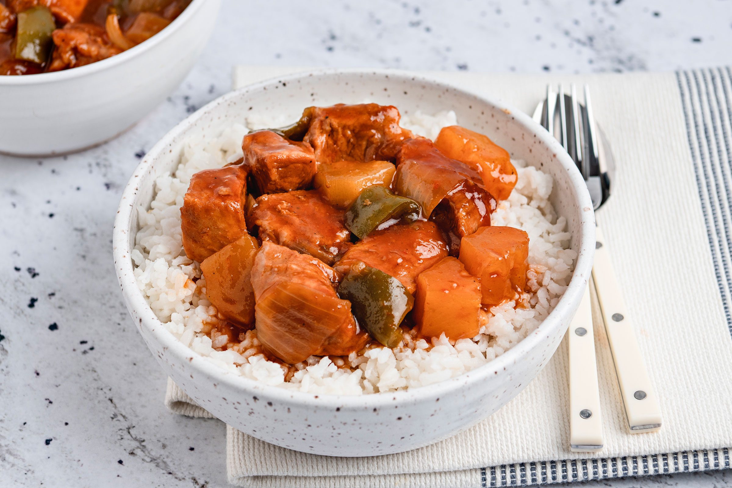 Slow Cooker Sweet And Sour Pork poured over rice in a bowl