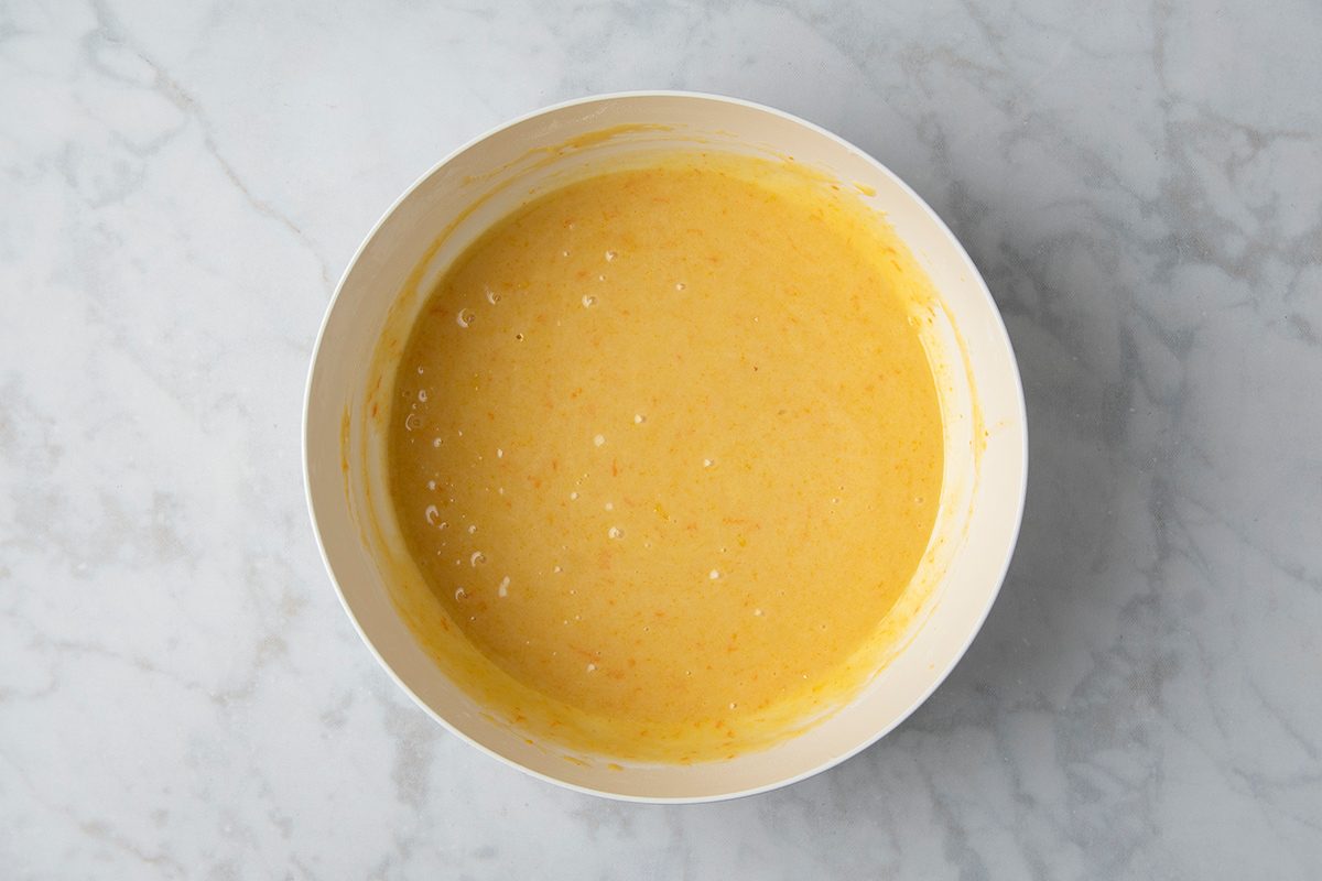 A white bowl filled with creamy yellow batter rests on a light marble surface.