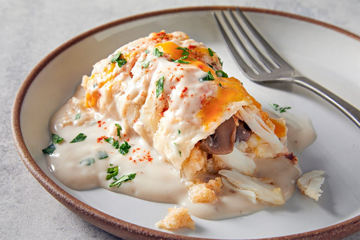 A plate with a serving of stuffed sole topped with creamy sauce, sprinkled with herbs and paprika, and a fork beside it.