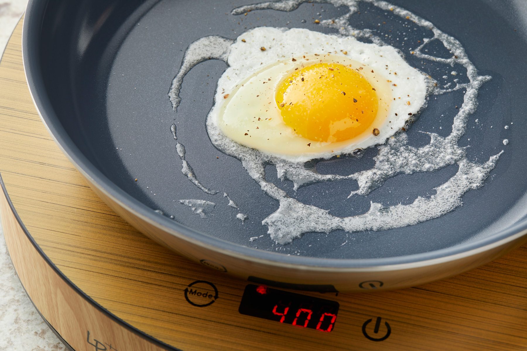 Close shot of crack eggs into the skillet; season with salt and pepper; induction; marble surface;