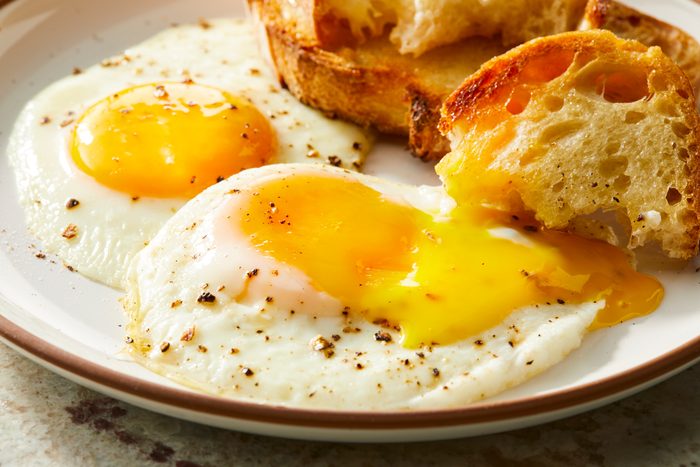Close up shot of Sunny Side Up Eggs; Served hot on a palte with breads slices; marble surface;
