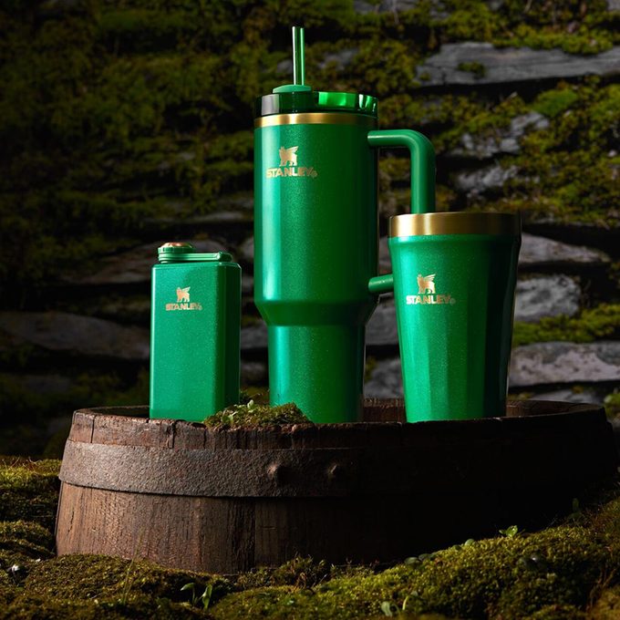 3 green Stanley St Patrick's Day drinking containers on a moss-covered barrel