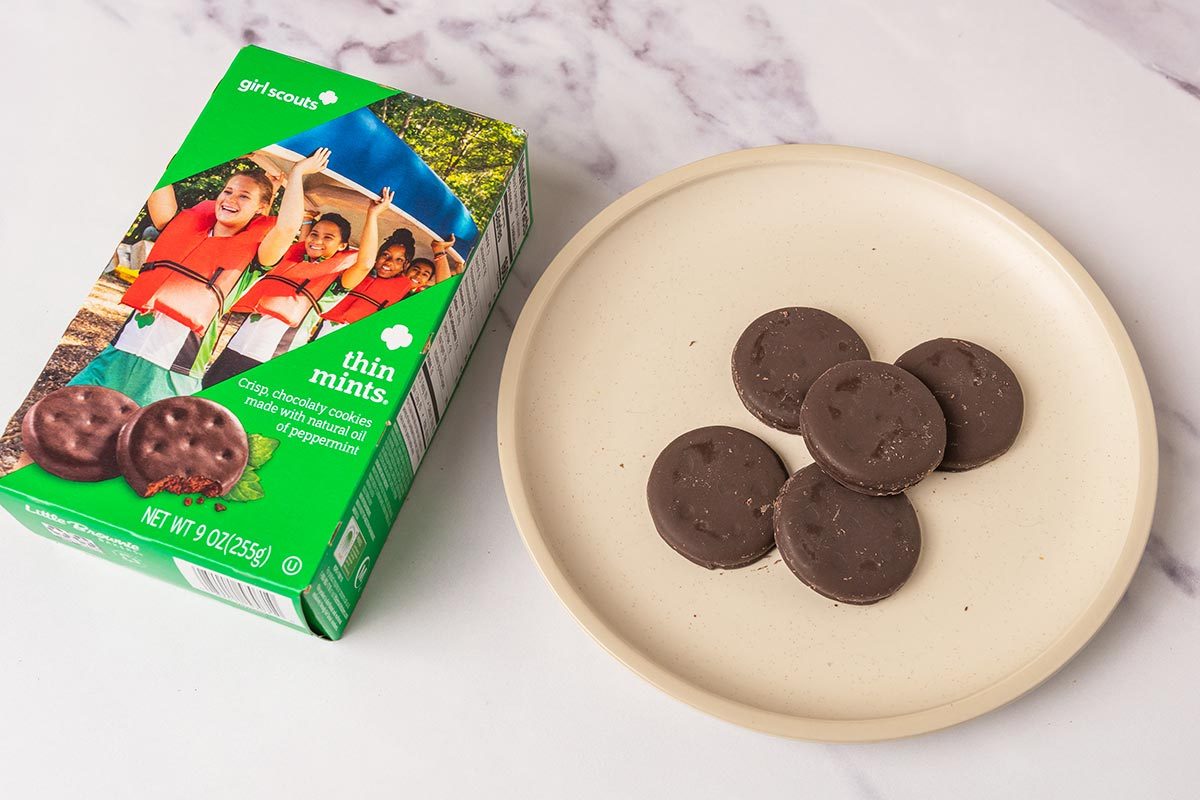 Package of Thin Mints Girl Scout Cookies next to several cookies on a plate