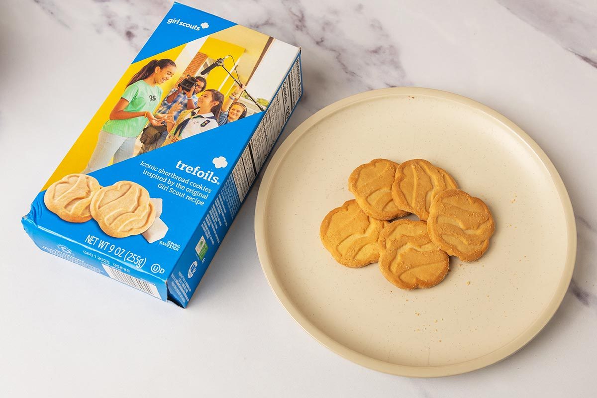 Package of Trefoils Girl Scout Cookies next to several cookies on a plate