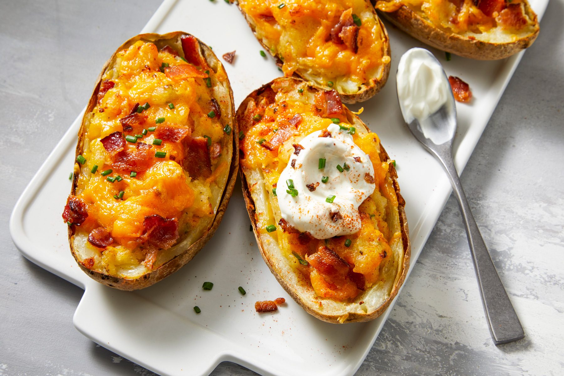 Overhead shot of Air-Fryer Twice Baked Potatoes topped with additional bacon and chives, dollops of sour cream and a sprinkle of paprika.