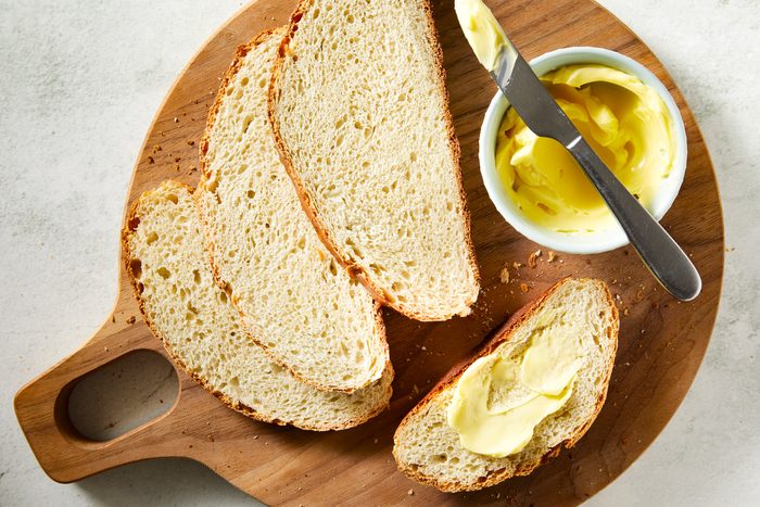 overhead shot of Banana Yeast Bread slices displayed on a wooden cutting board; with a small bowl filled with butter and knife is placed over it