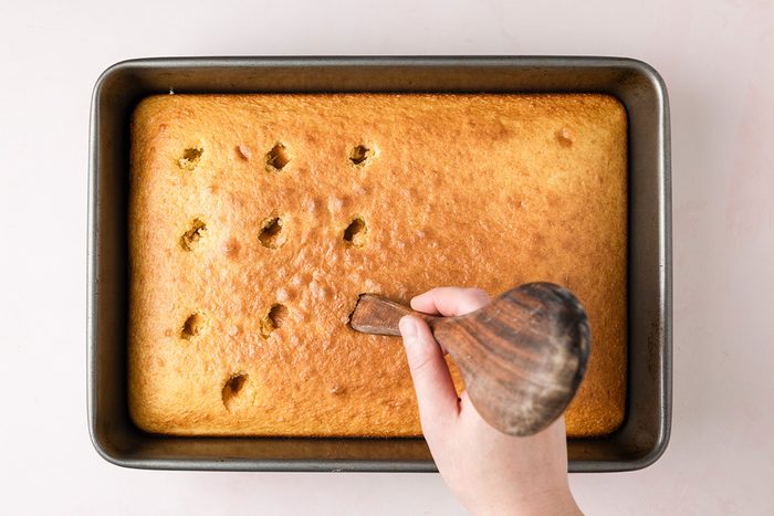 Boston Cream Poke Cake overhead shot of poked holes in cake with hand and spoon