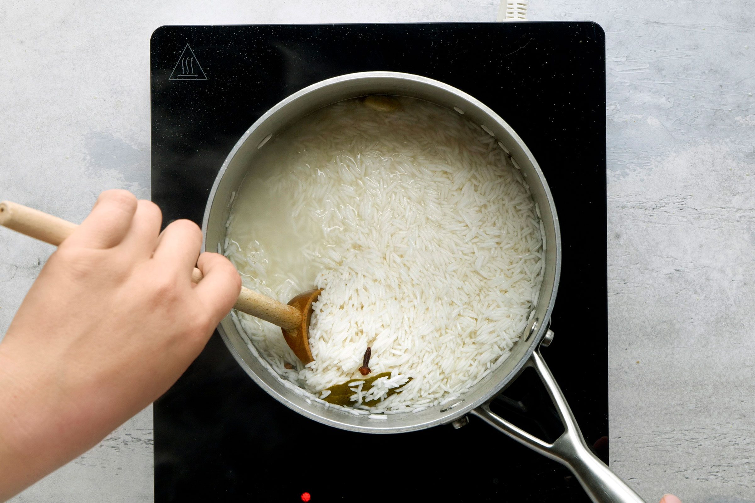 Boiling rice in a saucepan with warm water, salt and ghee, cardamom pod, bay leaf and cloves