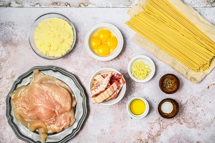 overhead shot of Chicken Carbonara Ingredients laid out in small bowls and plates on a grey concrete surface