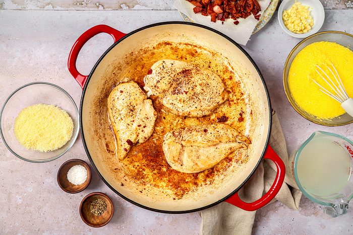 overhead shot of three cooked chicken breasts seasoned with spices, sitting in a light brown sauce at the bottom of the pot