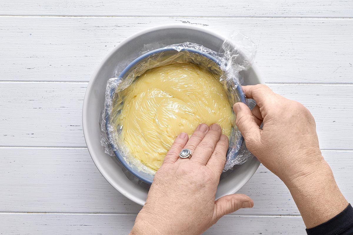 plastic wrap being pressed on pastry cream mixture