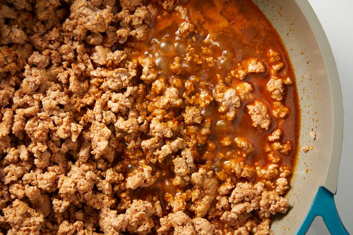 a closeup view of cooked ground meat in a skillet, featuring a mixture of crumbled light brown meat and a rich, reddish brown sauce that pools beneath it