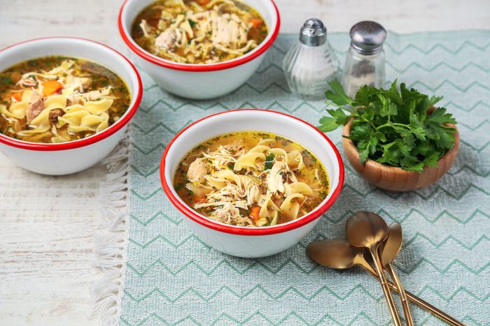 Cover push pull image of Taste of Home's Instant Pot Chicken Noodle Soup shot on a white wooden surface. Soup served in white and red enamel bowls with chopped fresh parsley as garnish; 3/4th