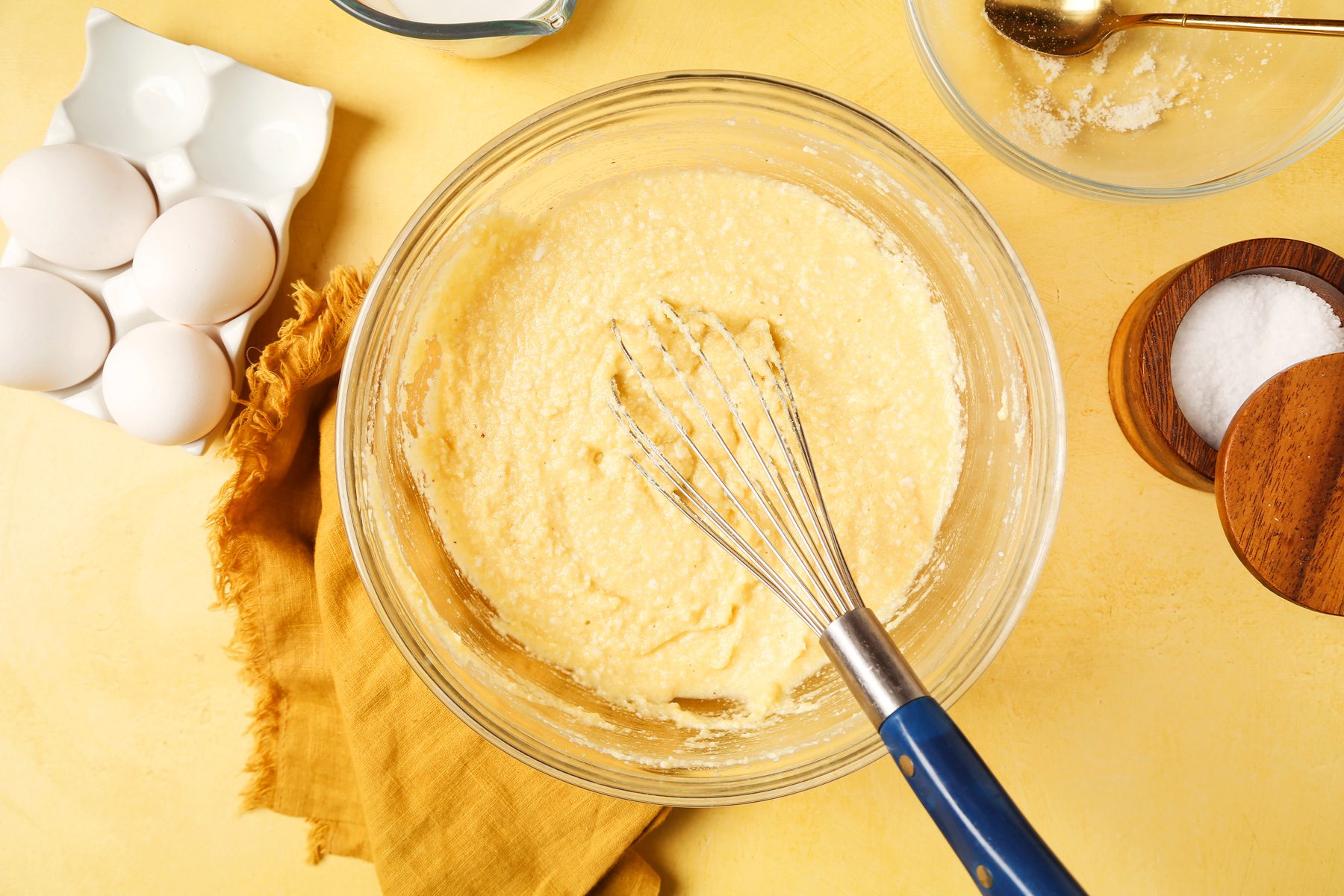 Keto Waffles shot on a yellow surface. Waffler batter mixed in a large mixing bowl with a whisk.