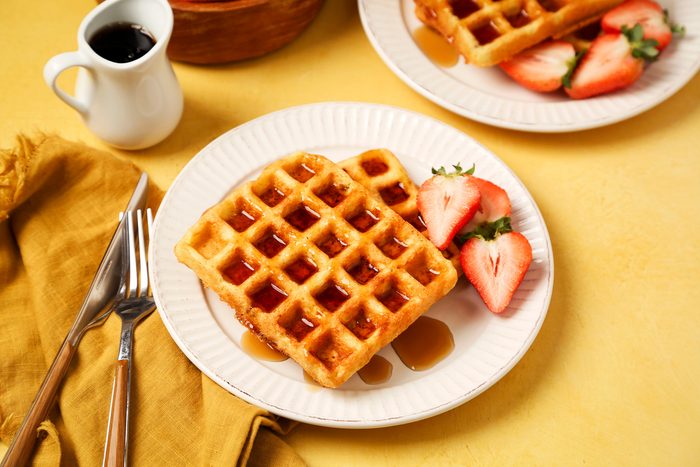 Keto Waffles shot on a yellow surface. Waffles served on a white plate with syrup and strawberries.