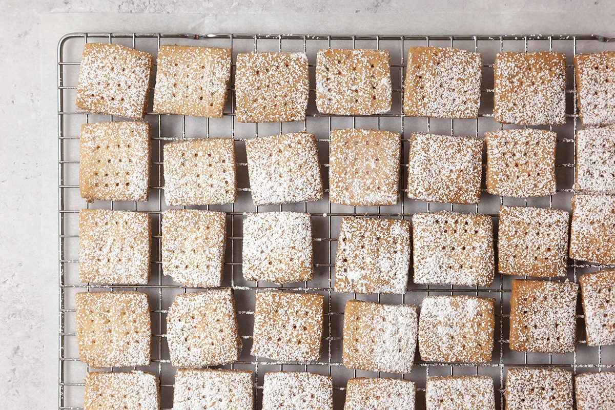 Square cookies with powdered sugar are arranged in rows on a wire cooling rack.
