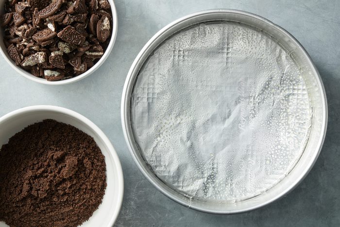 Overhead shot of a large bowl combine crushed cookies and butter; on a grey surface;