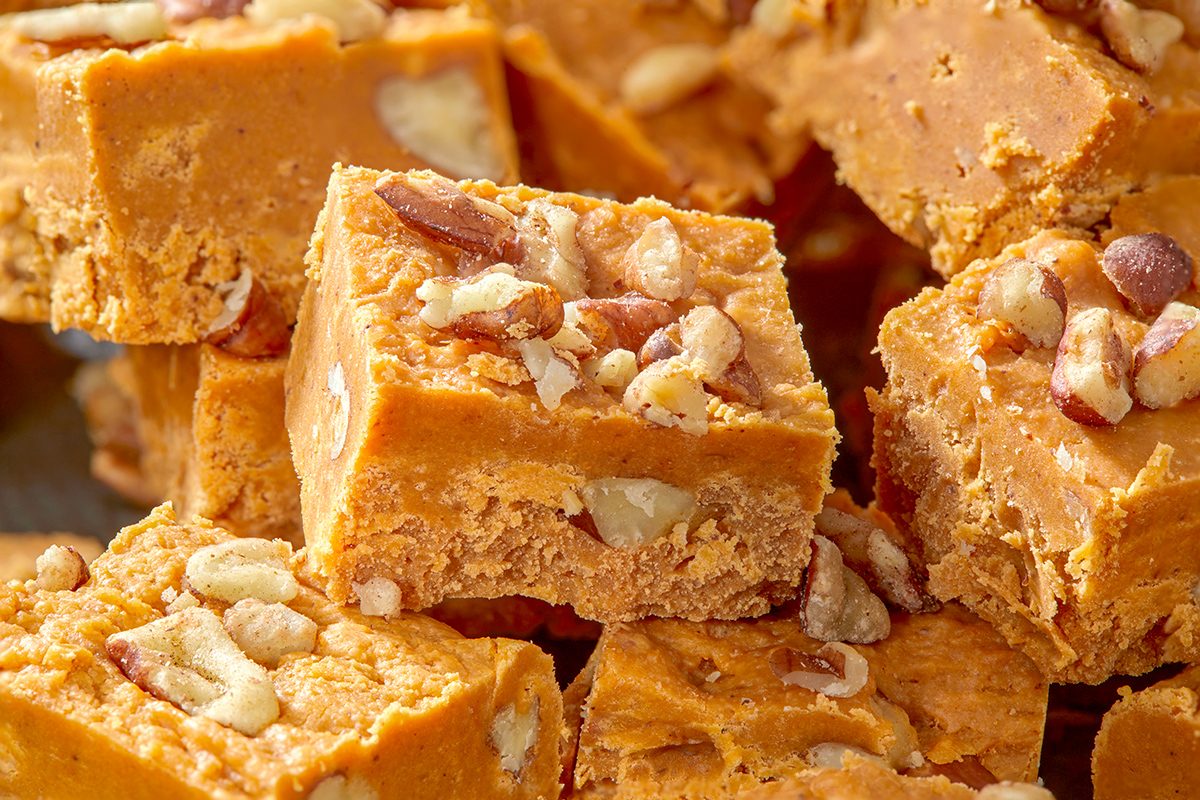 Close-up of several pieces of peanut butter fudge, each topped with chopped nuts. The fudge has a smooth, creamy appearance with a rich golden color, and the nuts add texture and contrast.