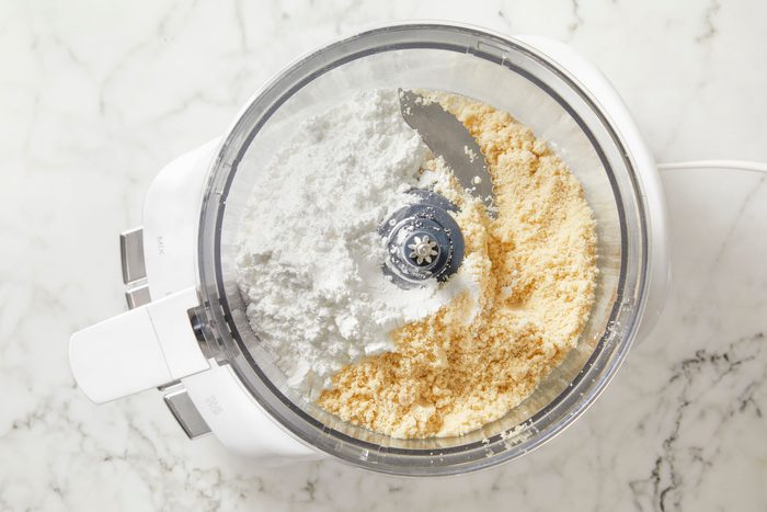 Overhead shot of place the almond flour and 1-3/4 cups confectioners’ sugar in a food processor; pulse until thoroughly mixed to ensure almond flour is very fine; on marble surface;