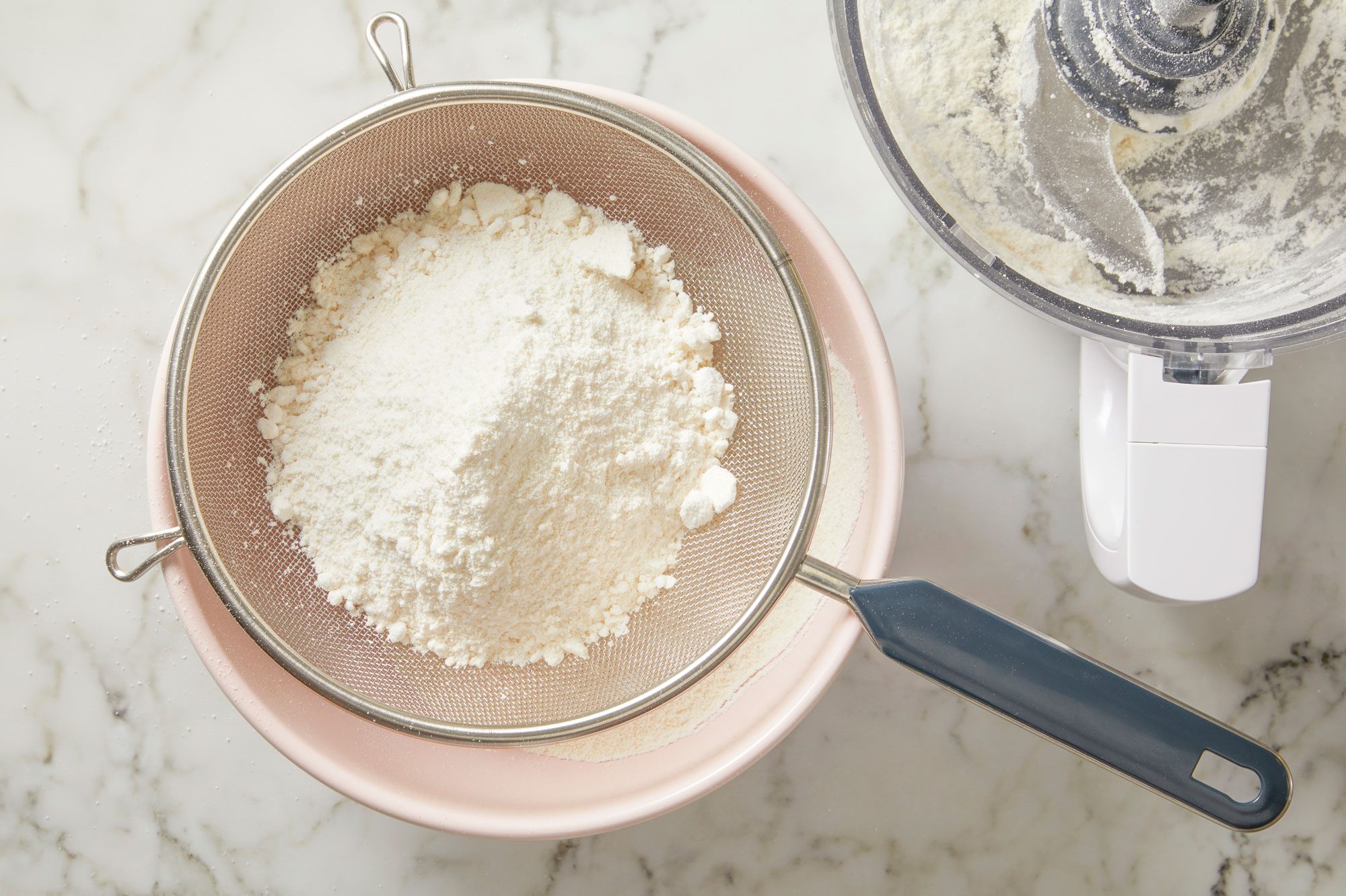 Overhead shot of pass almond flour mixture through a fine-mesh sieve; discard any large pieces that remain; on marble surface;