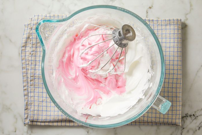 Overhead shot of the same egg white mixture bowl over a napkin; add in enough food coloring to achieve desired color; whisk tool; marble surface;
