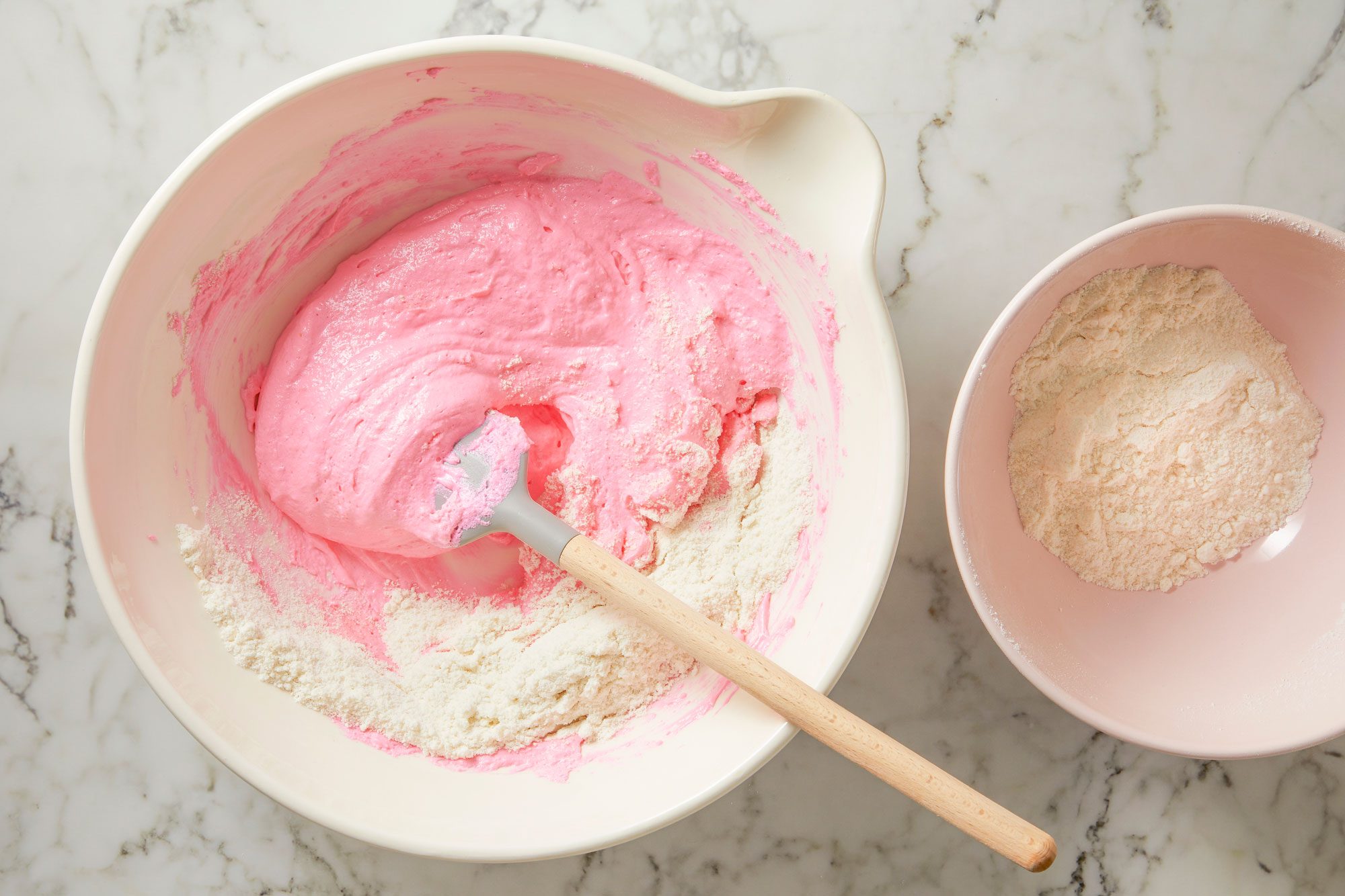 Overhead shot of gently fold the almond flour mixture into meringue; a third at a time; using the side of a spatula; smooth batter up sides of bowl several times to remove air bubbles and ensure there are no lumps; do not over mix; marble surface;