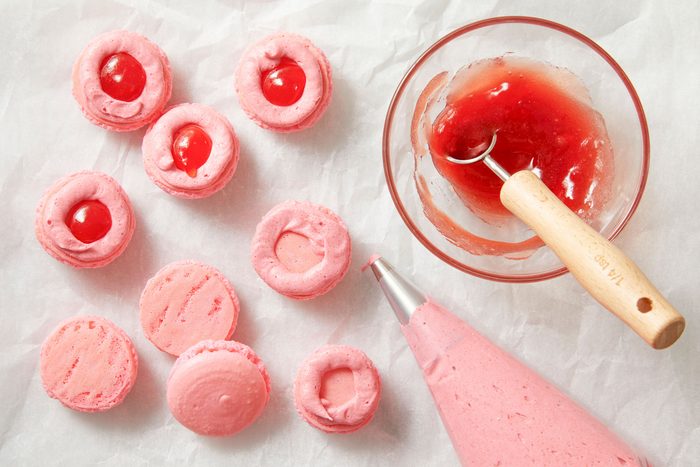 Overhead shot of pour frosting into a pastry bag fitted with a small round tip; pipe a circle of buttercream onto the bottoms of half the macarons; Place 1/4 teaspoon strawberry jam in center of each frosting circle; Top with remaining macaron shells; refrigerate covered until ready to serve;